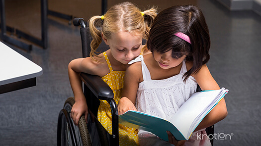 Dos niñas viendo un libro, una de ellas tiene una discapacidad